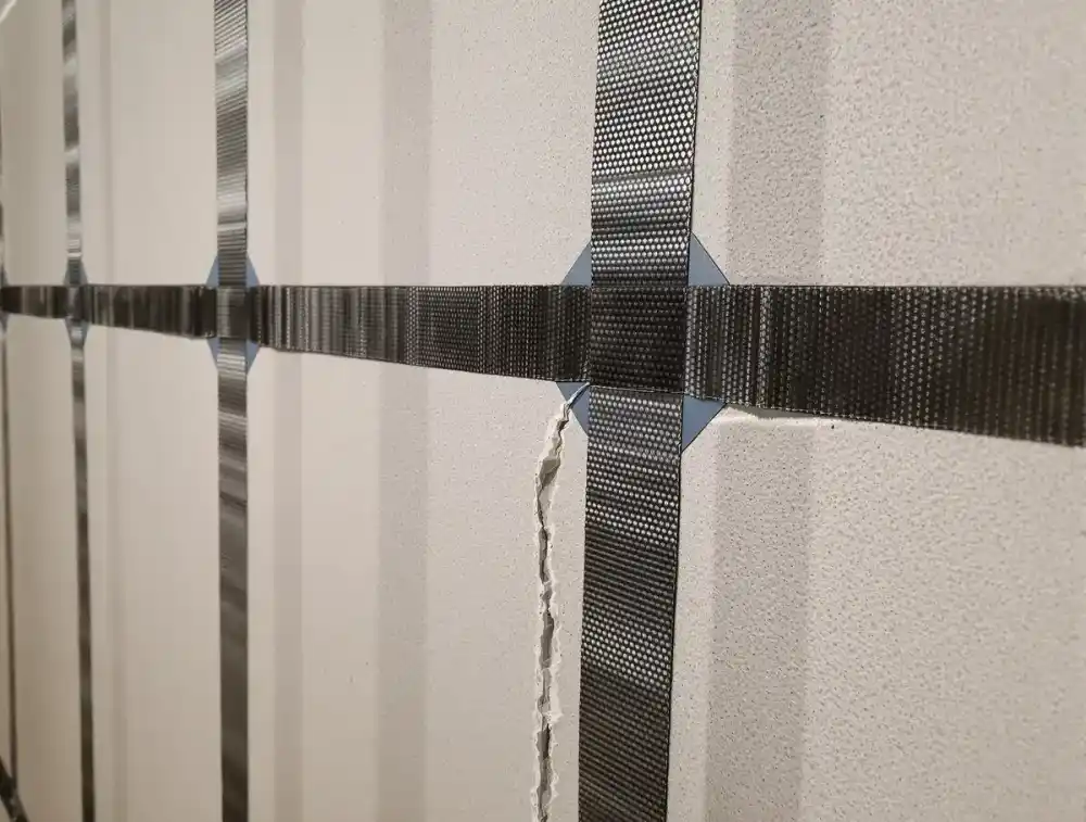 Carbon fiber straps bonded vertically to a concrete block basement wall with structural epoxy, reinforcing a horizontal crack to prevent further inward bowing from lateral soil pressure — a non-invasive alternative to wall anchors for early-stage deflection