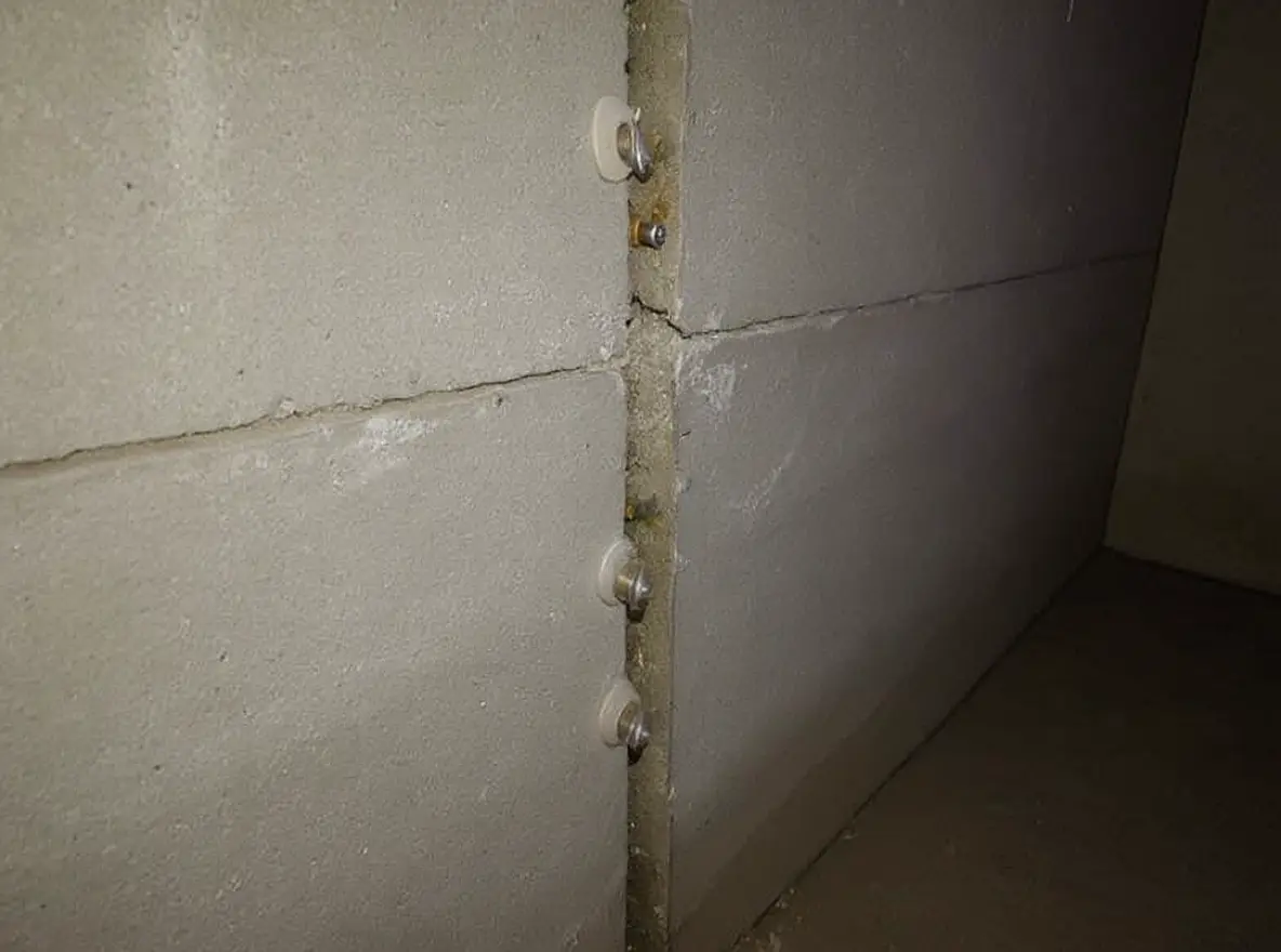 Epoxy crack injection ports installed at 6-inch intervals along a vertical crack in a poured concrete basement wall, with amber epoxy visible filling the crack from inside out