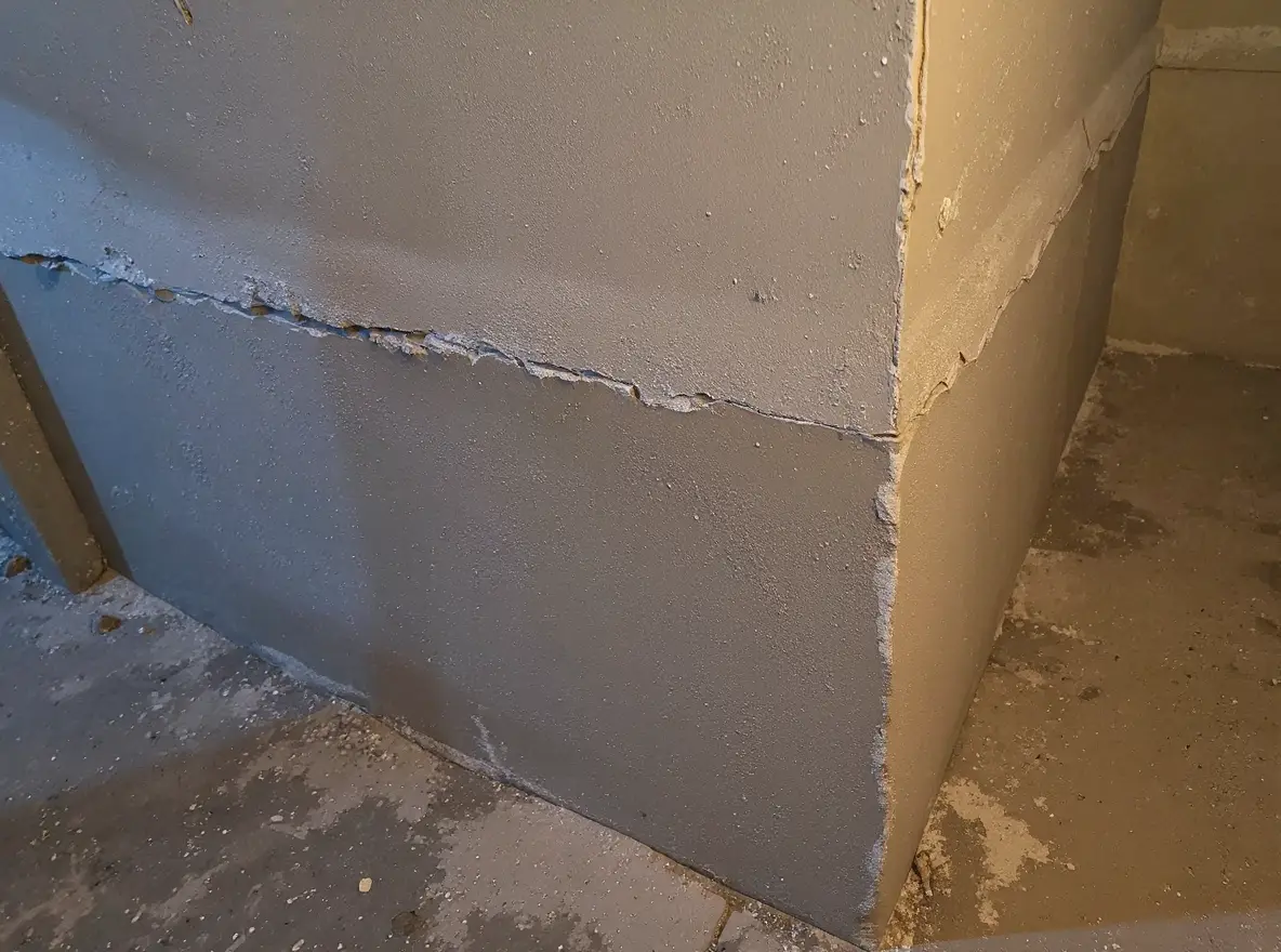 Completed epoxy crack injection repair in a poured concrete wall with ports removed and surface sealed smooth — the repaired crack is barely visible as a thin line