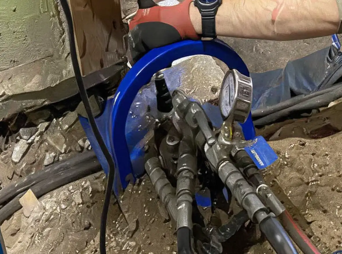 Close-up of a push pier bracket assembly permanently bolted to a concrete foundation footing showing the lock-off mechanism after installation with the pier tube extending into soil