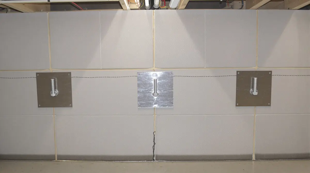 Wall anchor system installed on a bowing concrete block basement wall with steel rod extending through the wall and soil to a buried earth anchor plate 10-15 feet away, counteracting lateral soil pressure from Midwest expansive clay