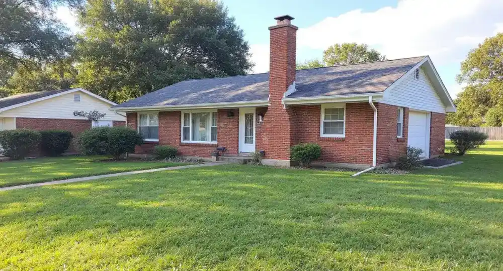 Full exterior view of a ranch home chimney leaning away from the house wall with visible gap at the roofline, demonstrating progressive differential settlement