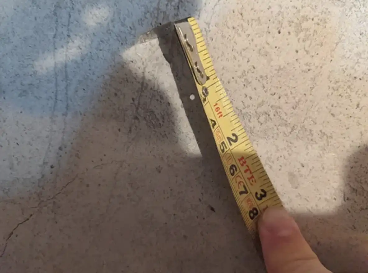 Diagonal crack at 45 degrees extending from a basement window corner in poured concrete, widening from hairline to 3/16 inch with visible displacement indicating differential settlement