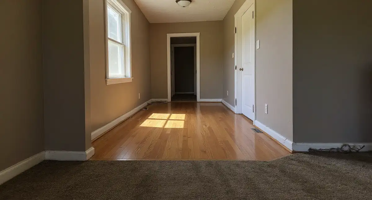 Interior hallway of a mid-century home showing visible floor slope with baseboard separation at floor level and crooked door frame from differential foundation settlement
