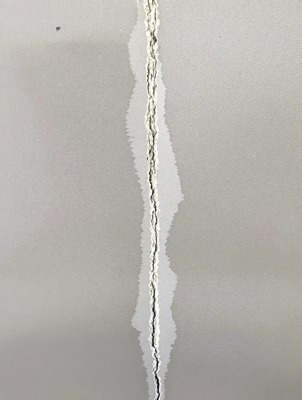 Vertical crack running floor-to-ceiling in a poured concrete basement wall with uniform hairline width, typical of concrete curing shrinkage rather than active structural settlement — less urgent than horizontal or stair-step patterns but worth monitoring for width changes